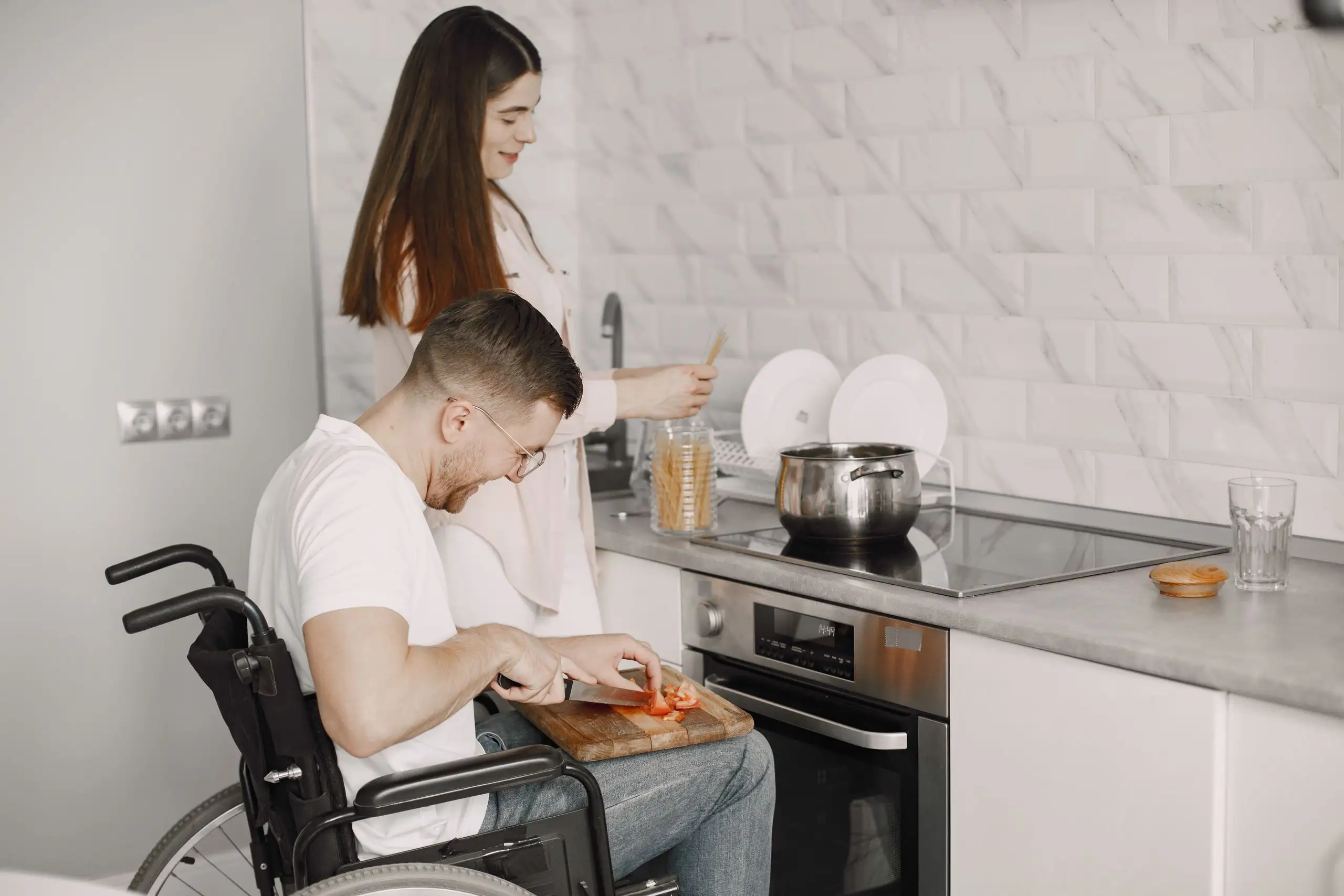 A man in a wheelchair and a woman cooking together in a bright kitchen