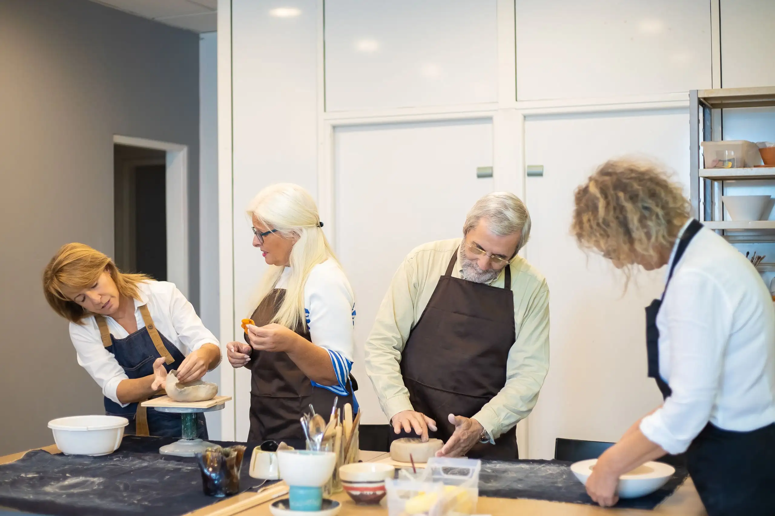 Adults of different ages shaping clay together at a pottery workshop