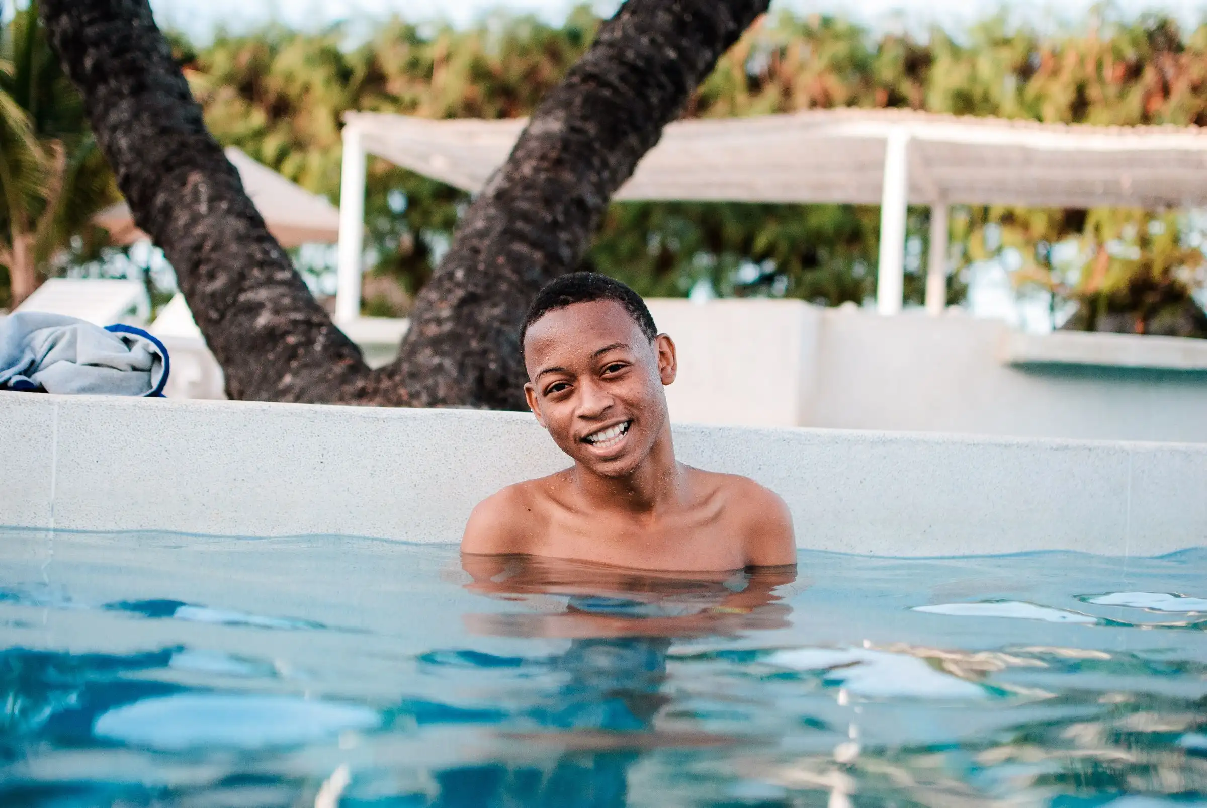 A smiling man resting at the edge of an outdoor swimming pool
