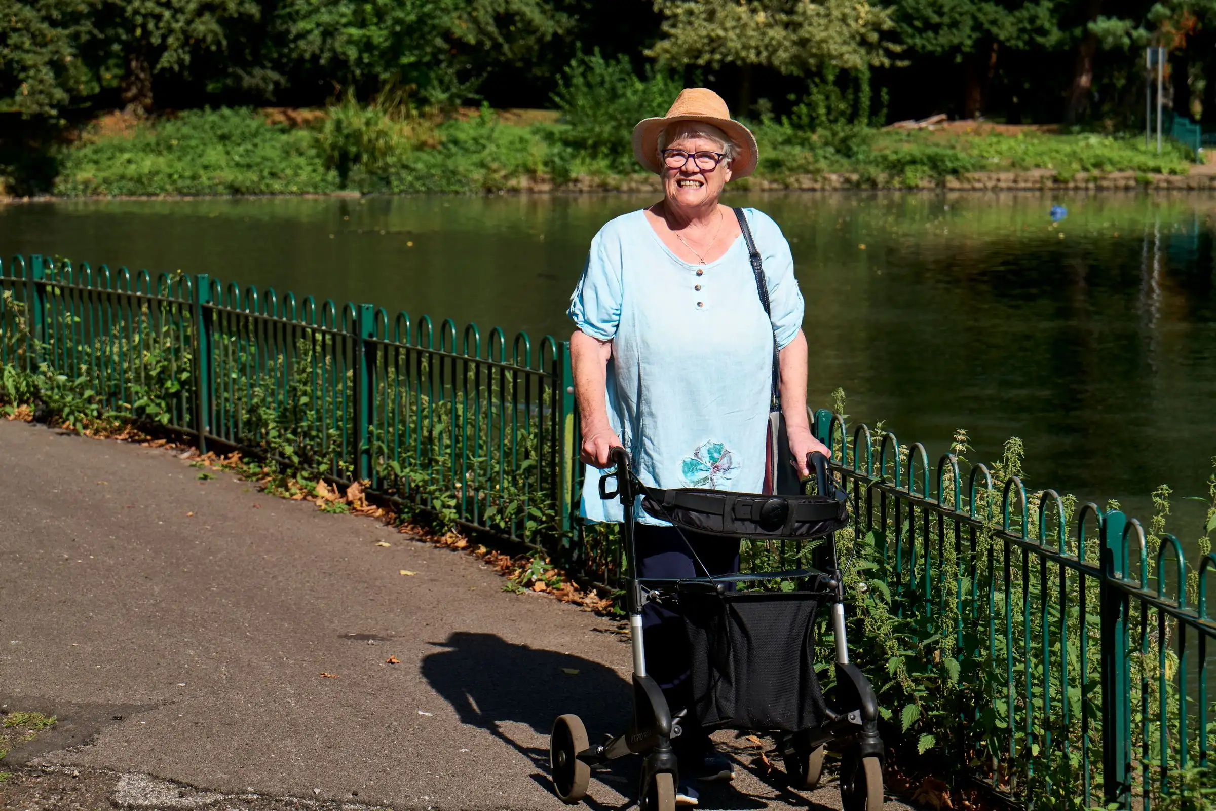 An older woman with a walking frame on a path beside the water